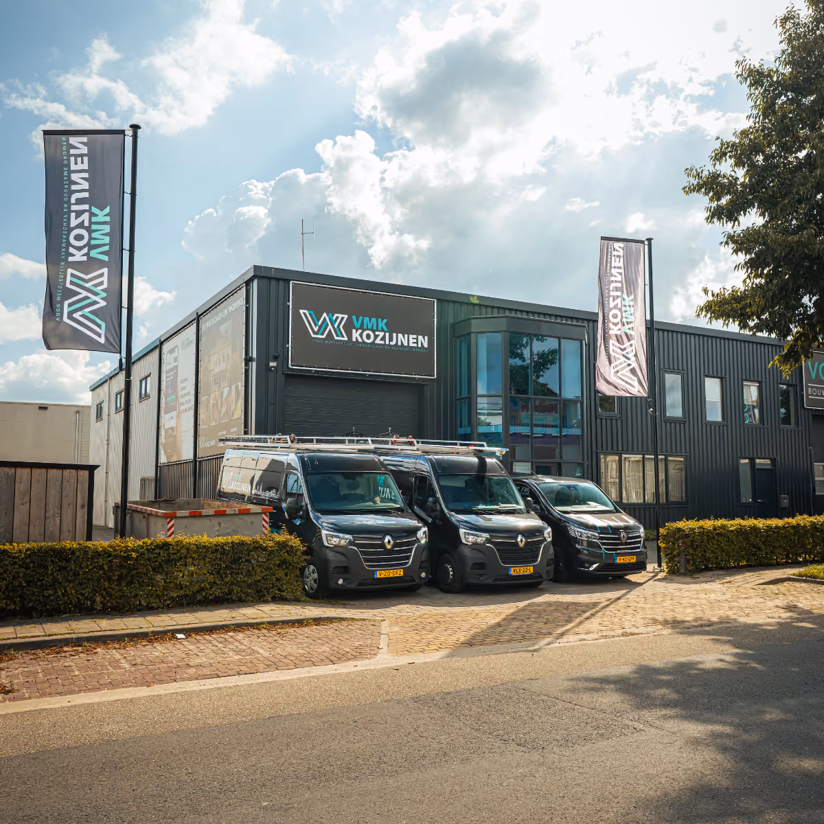 Drie zwarte bestelwagens geparkeerd voor een modern bedrijfsgebouw met VMK Kozijnen borden en vlaggen.