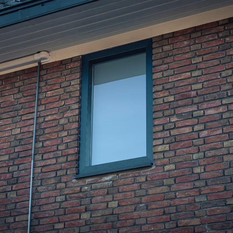 Donkergroen kozijn met groot glas in een rode bakstenen gevel.