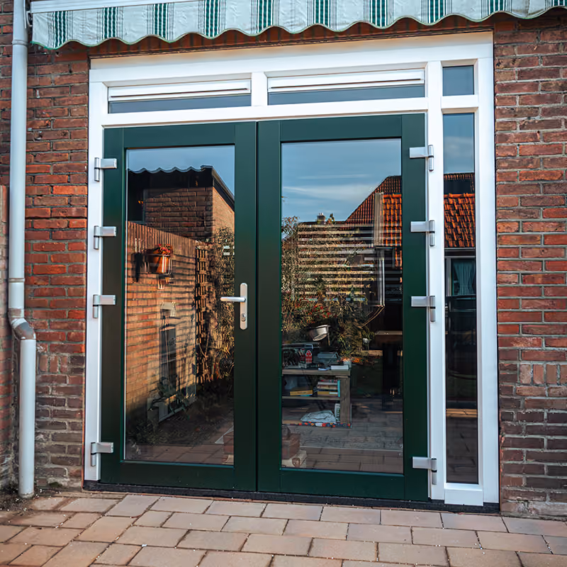 Donkergroene dubbele openslaande deuren met glas in een metselwerk gevel en zonnescherm erboven.