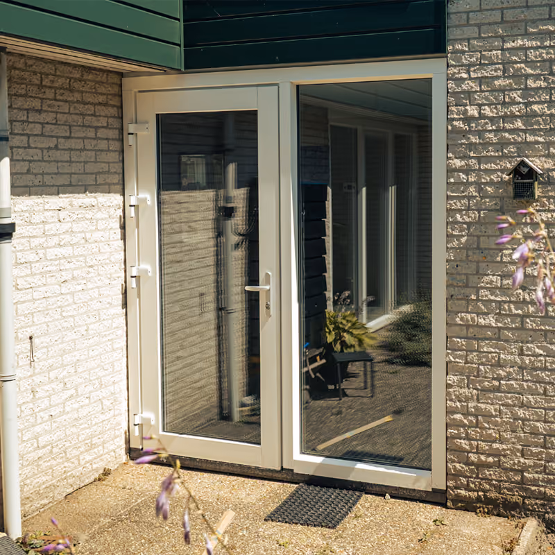 Open witte dubbele deur met glas in een bakstenen buitenmuur en buitentapijt.