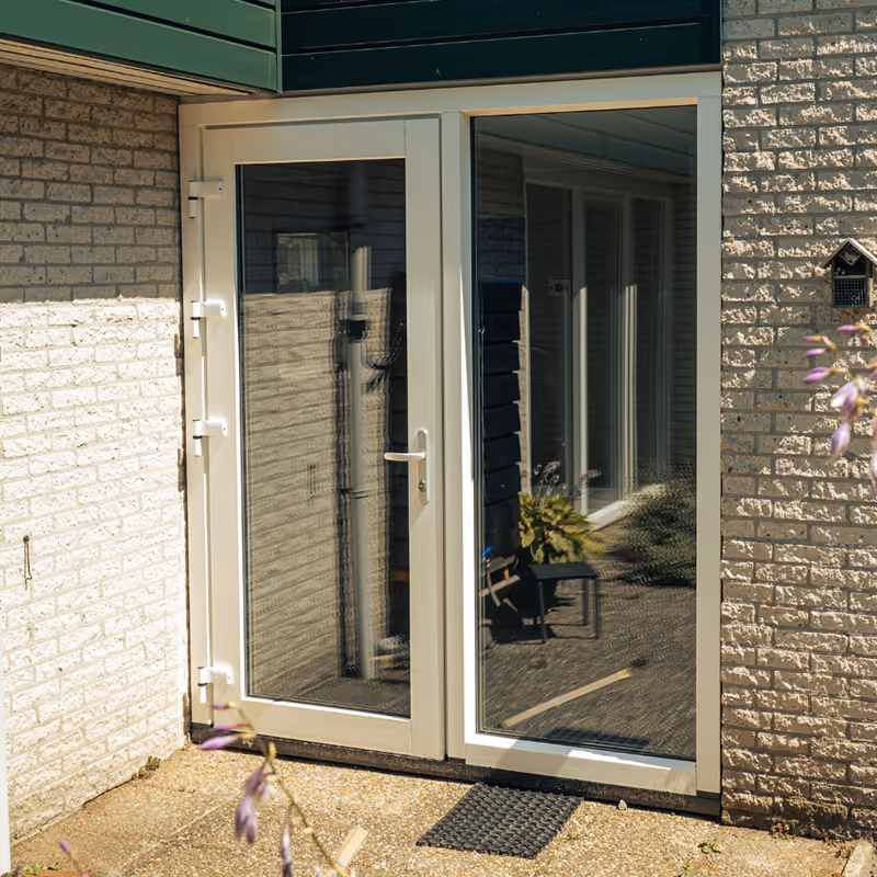 Witte dubbele glazen deur van kunststof met mat op betonnen terras bij huis met bakstenen muren.