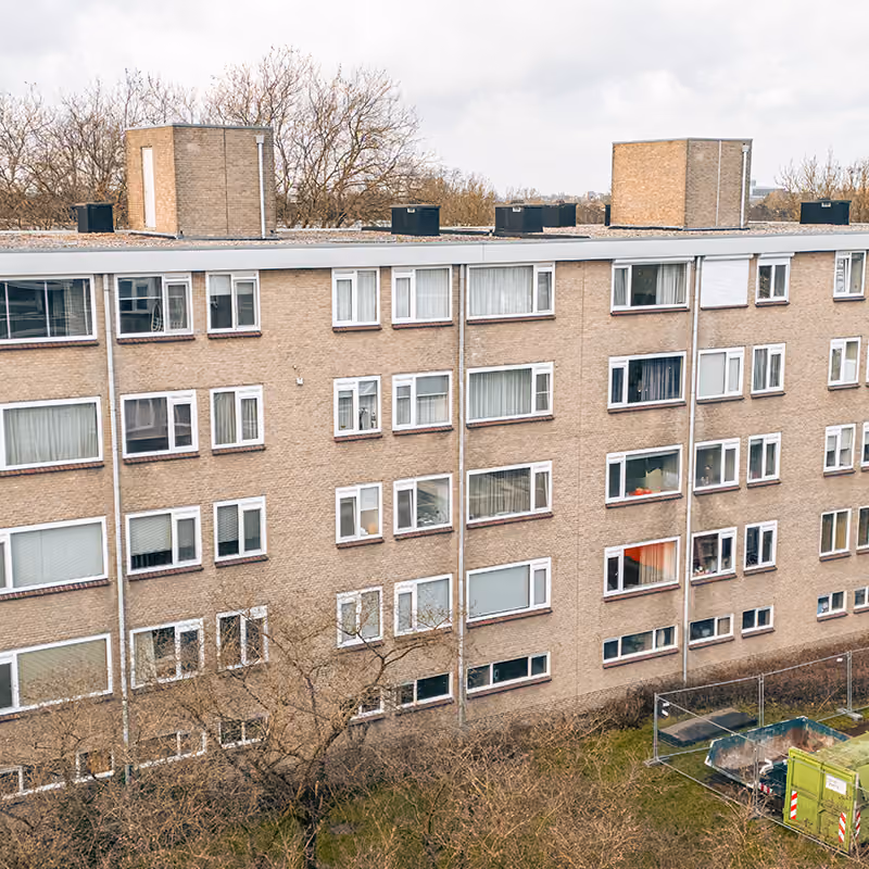 Gevel van een appartementscomplex met kunststof kozijnen en ramen, bomen eromheen.