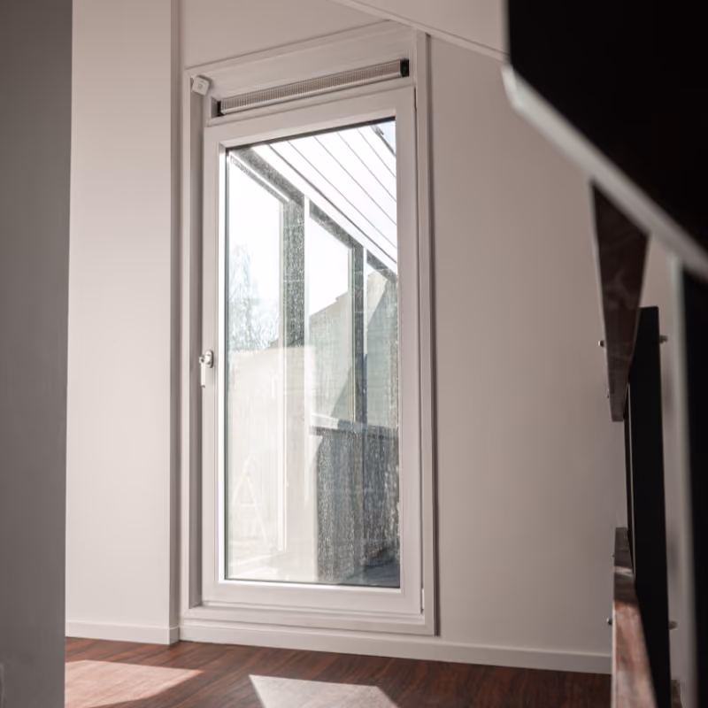 Een moderne glazen deur met wit frame in een minimalistisch interieur met houten vloer en wit geschilderde muren.