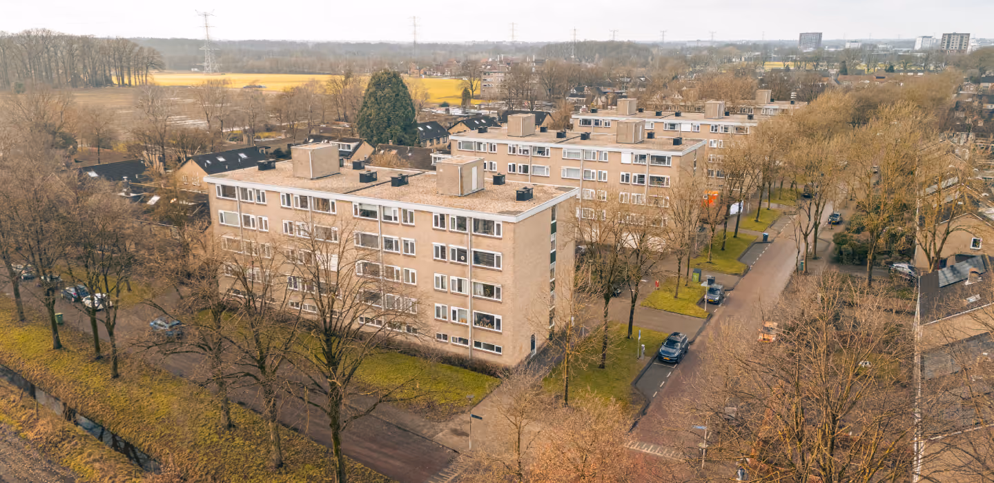 Luchtfoto van een woonwijk met twee- en drielaagse appartementen omgeven door kale bomen en een rustige straat in de herfst.