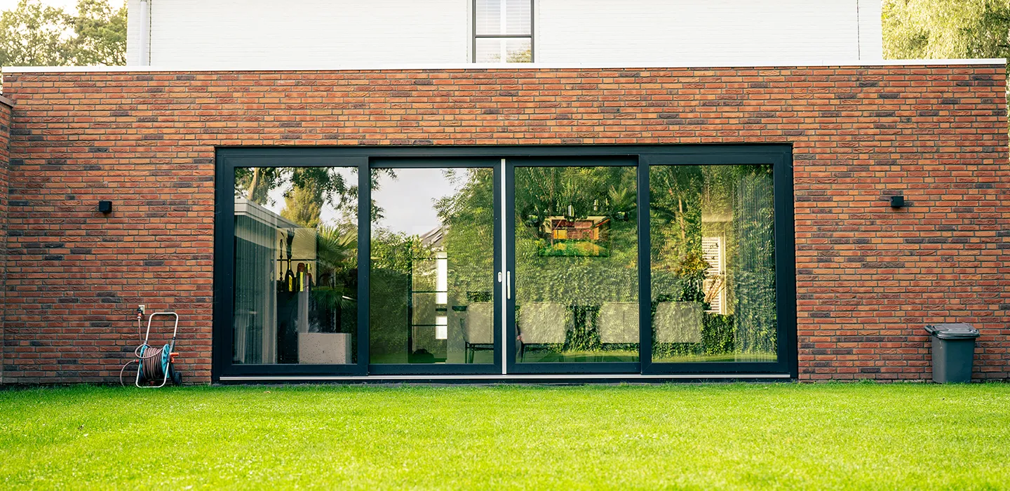 Antracieten 4-delige kunststof schuifpui in een bakstenen gevel met uitzicht op de tuin