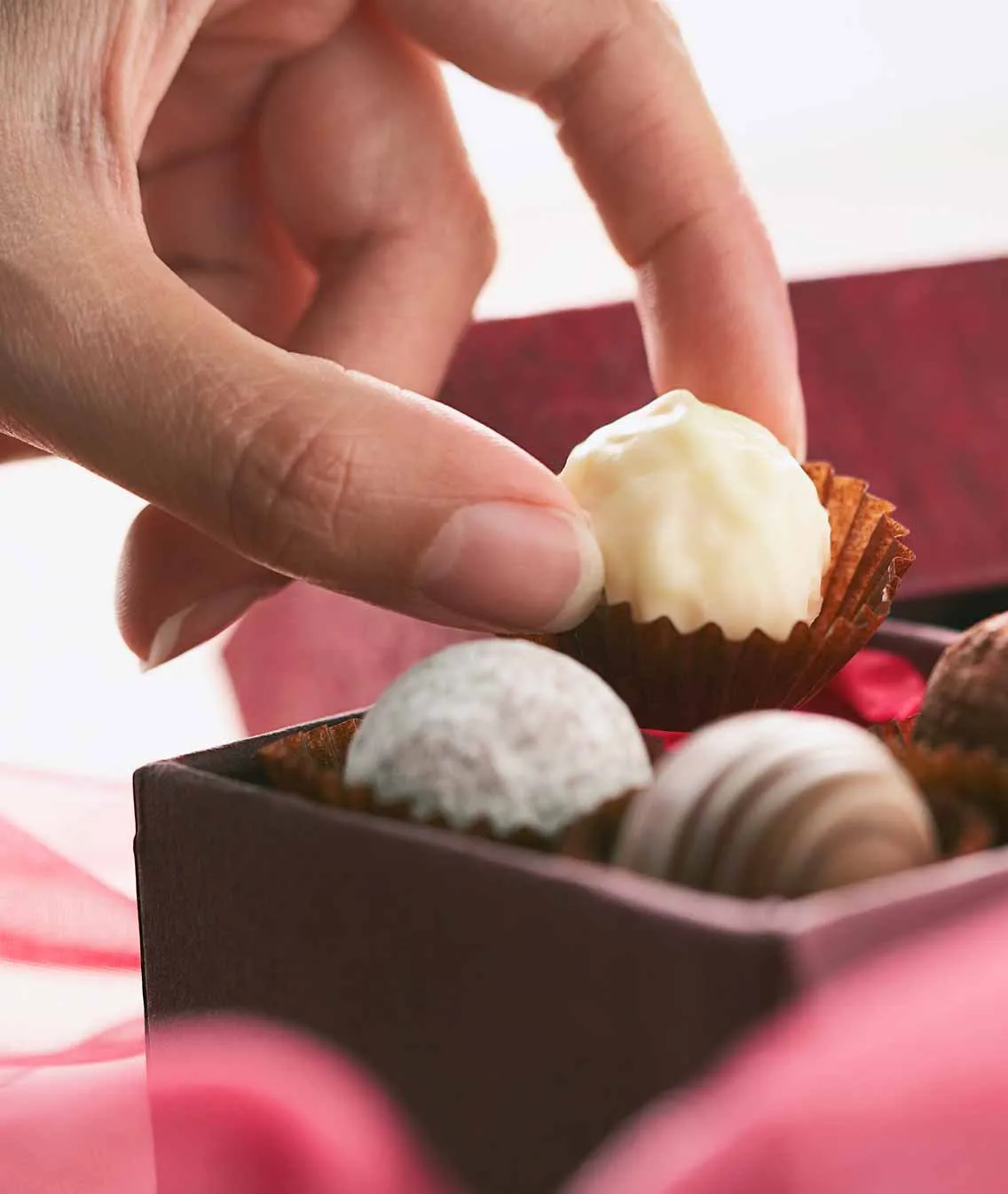 Eine Hand greift nach einer weißen Praline aus einer edlen Schachtel mit verschiedenen handgemachten Pralinen.