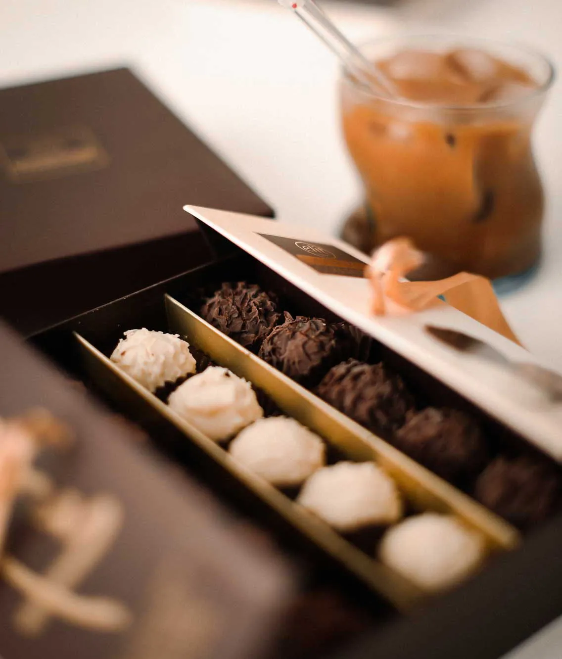 Geöffnete Pralinenschachtel mit edler Verpackung, gefüllt mit einer Reihe weißer und einer Reihe dunkler Schokoladenpralinen – luxuriöse Pralinenmischung als Geschenk oder Genussmoment.