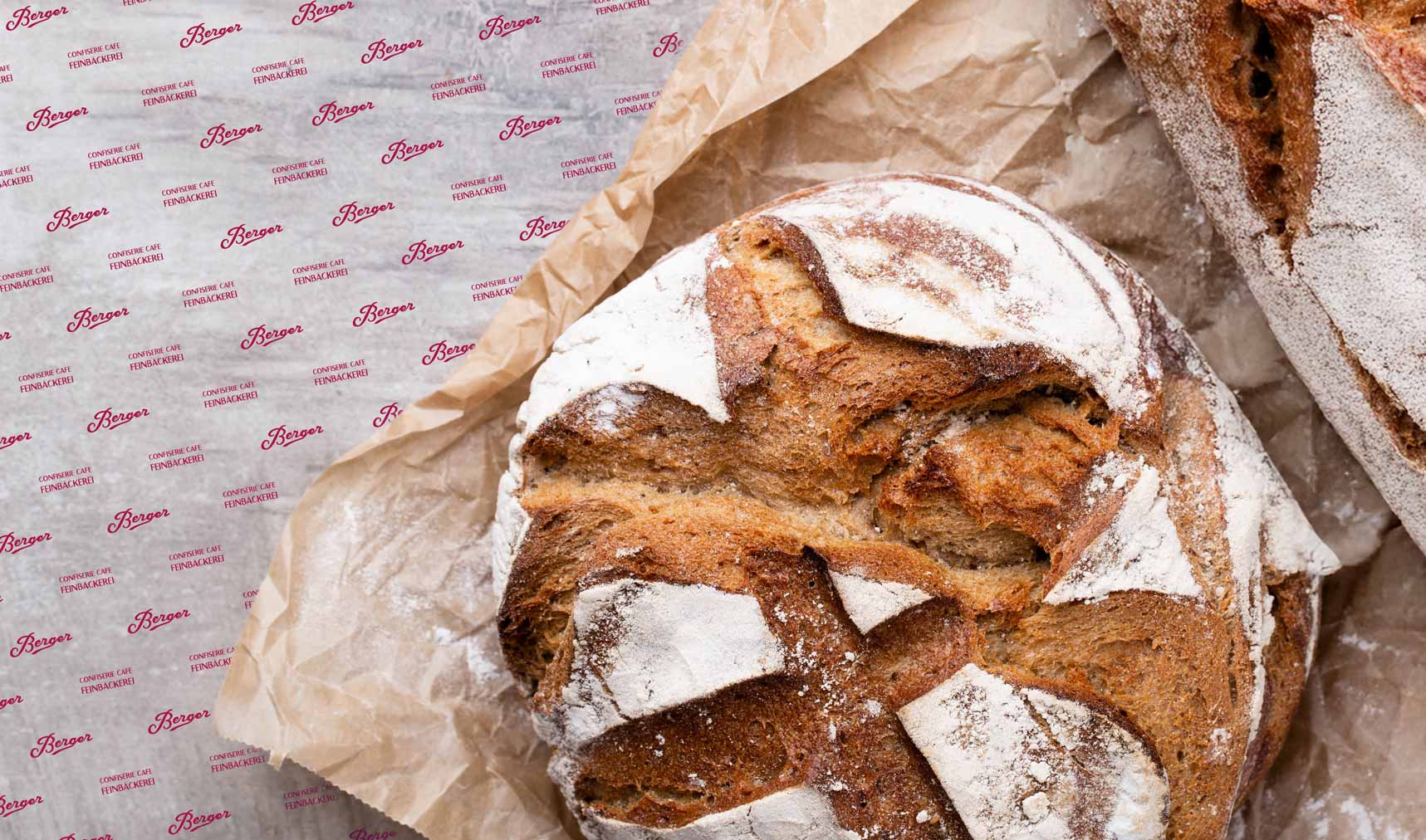 mit Mehl bestäubtes Brote liegen nebeneinander auf einem braunen Brotpapier auf einem grauen Tisch.