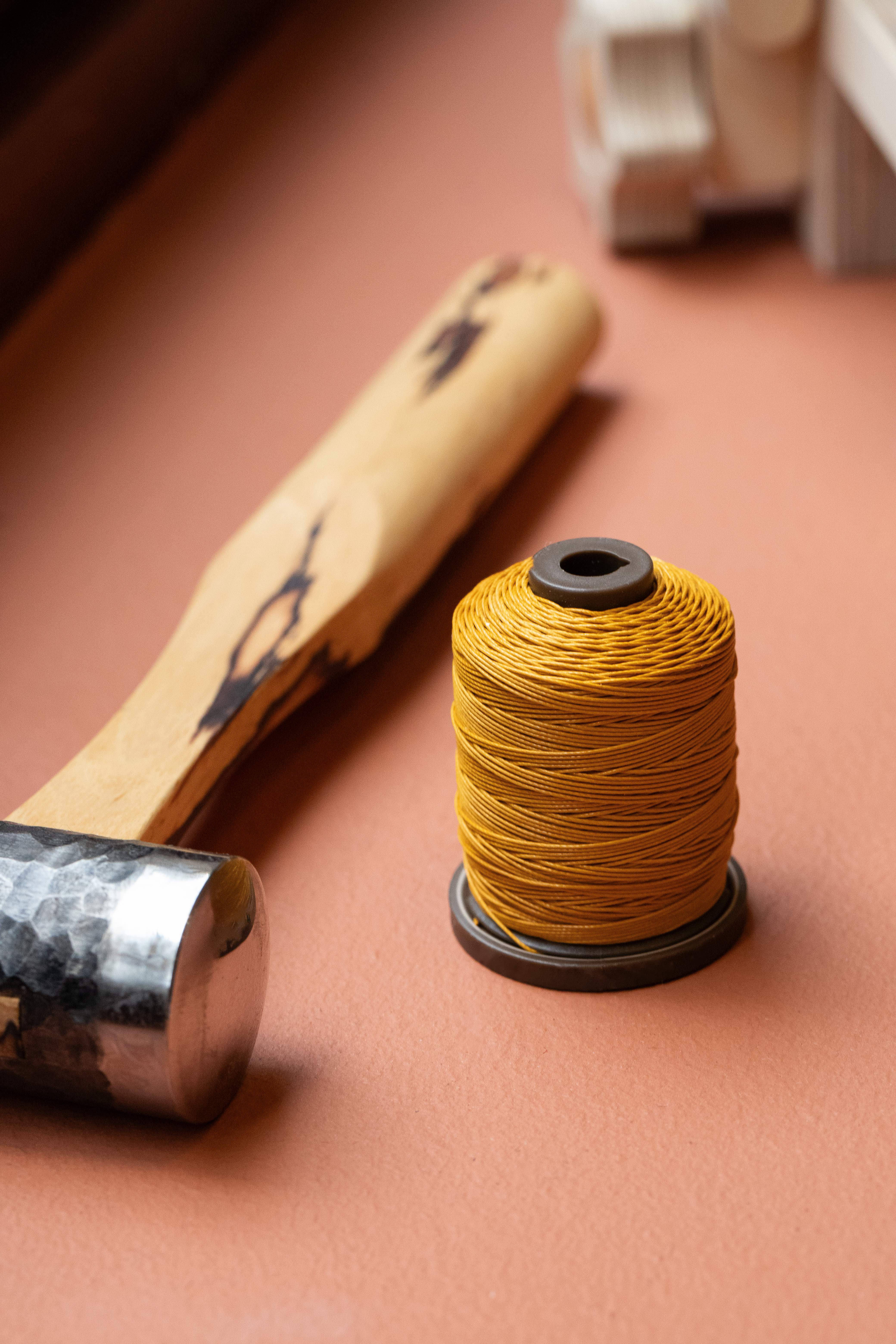 Spool of yellow thread on a peach-colored surface next to a small hammer and a metal tool in Braceletiers akrivia strapmaking workshop in Geneva