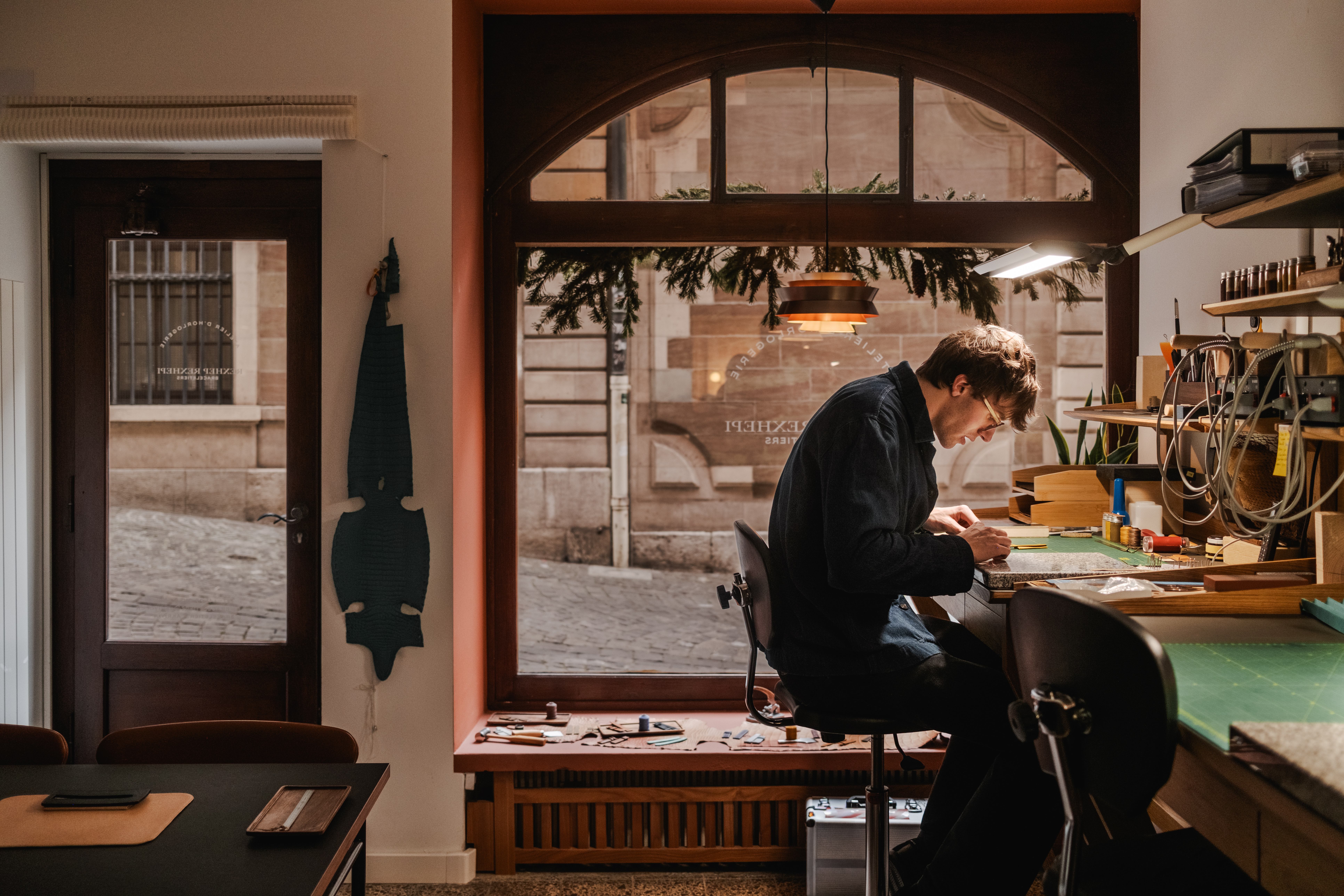 Leather artisan working at his bench in Braceletiers Akrivia workshop and hand-sewing a strap