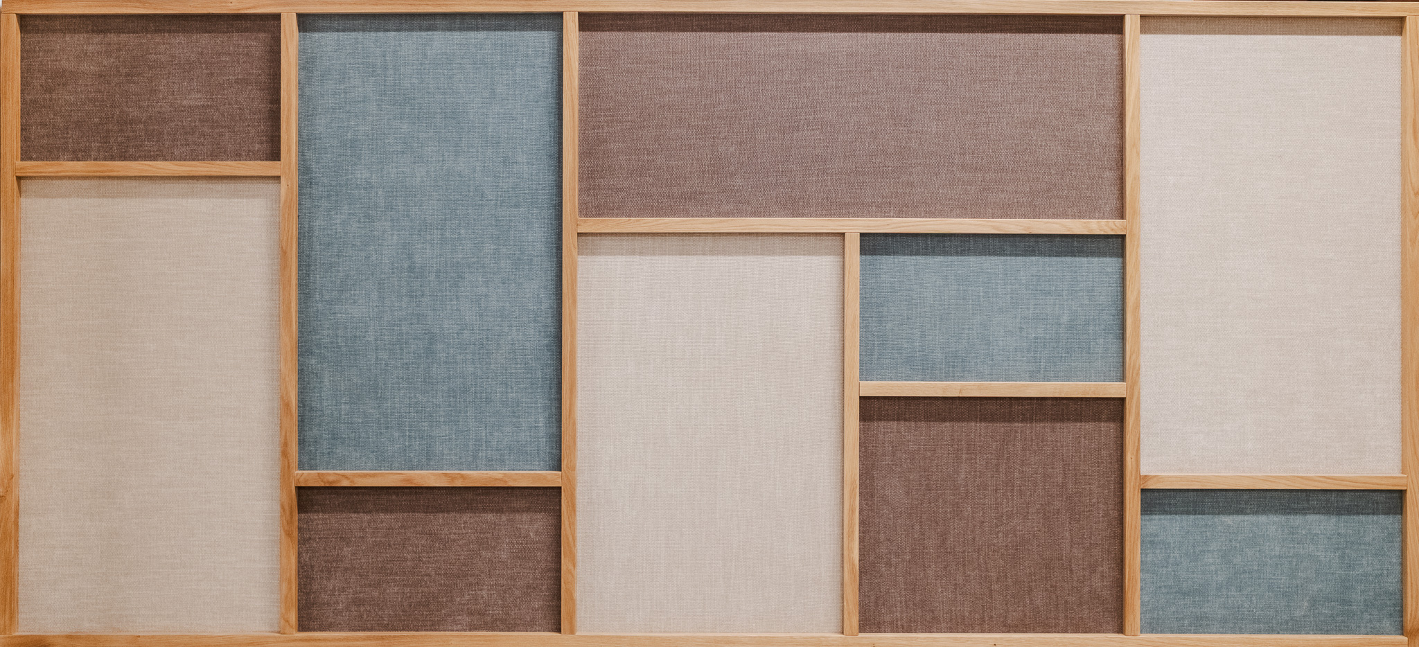Wooden grid wall panel filled with rectangular fabric sections in neutral, blue, and brown tones.