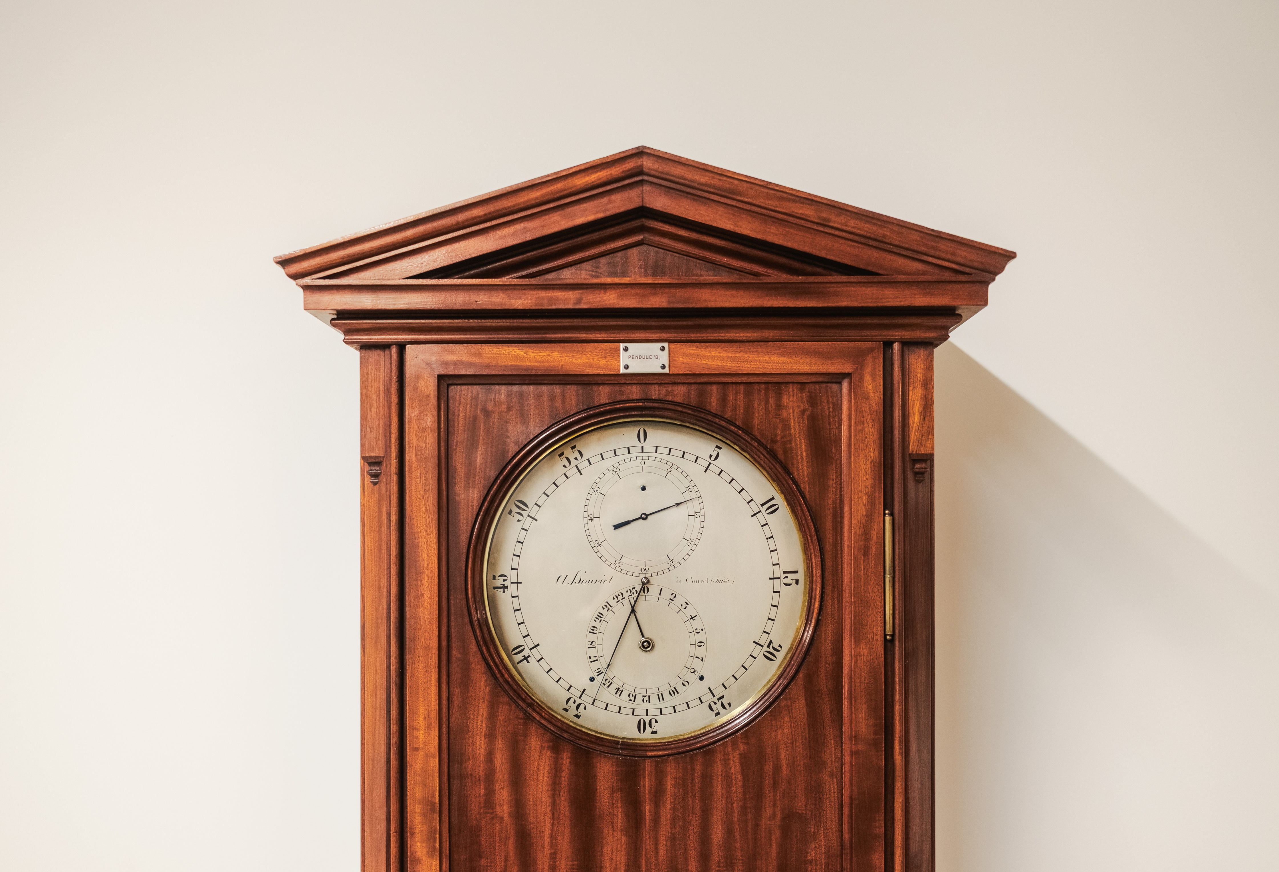 Antique wooden wall clock with a round white dial and triangular pediment in Rexhep Rexhepi's workshop in Geneva