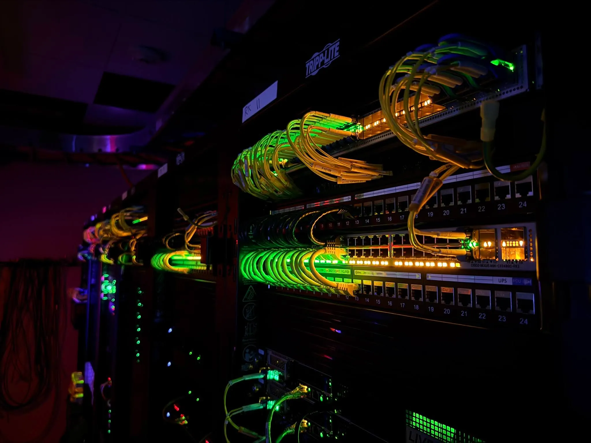 Fiber optic and data cables glowing in a dark server rack, illustrating ST-2110 IP broadcast core networking.