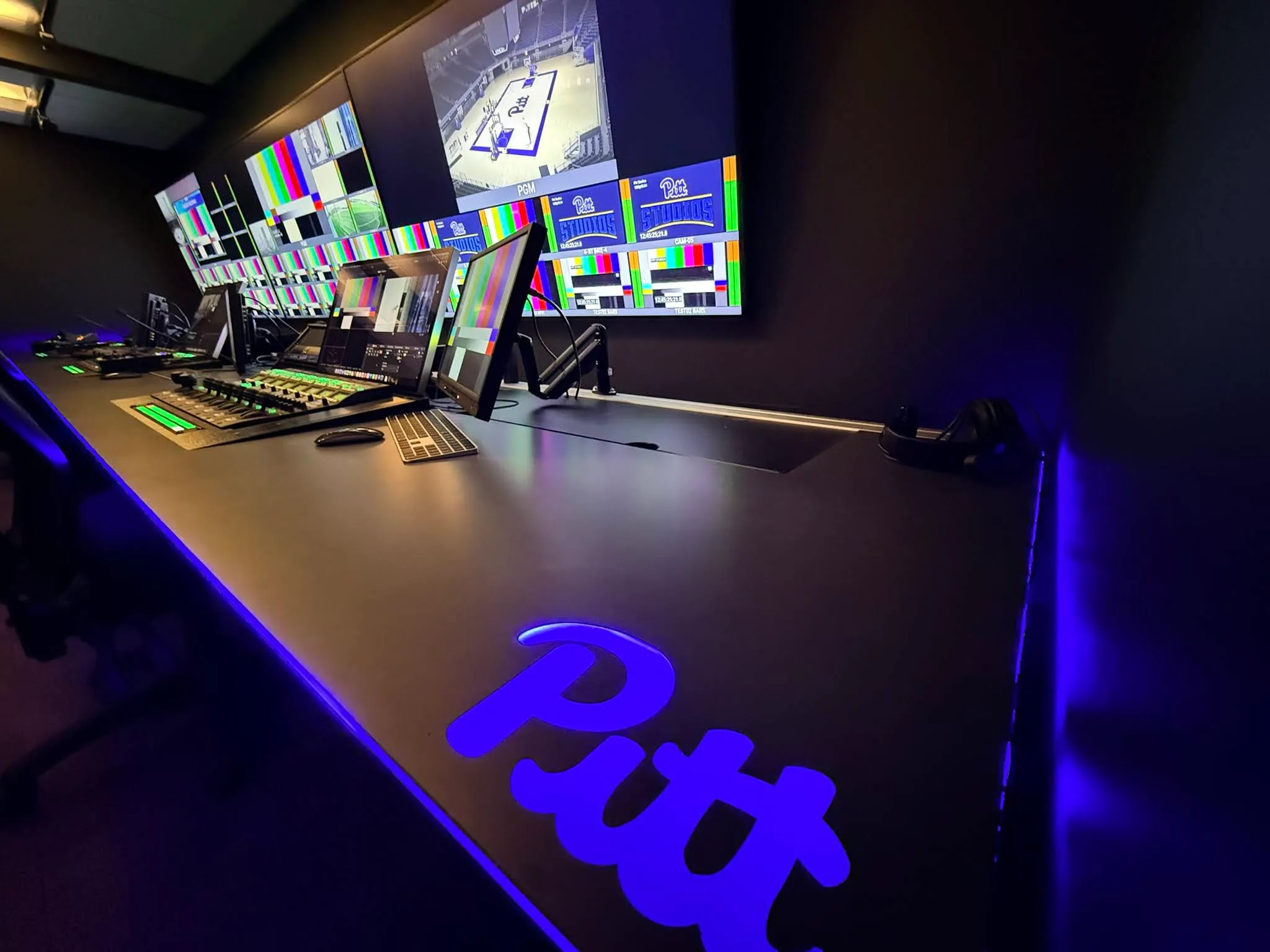 Custom control room desk with glowing blue Pitt logo and a wide monitor array for college sports broadcasting.