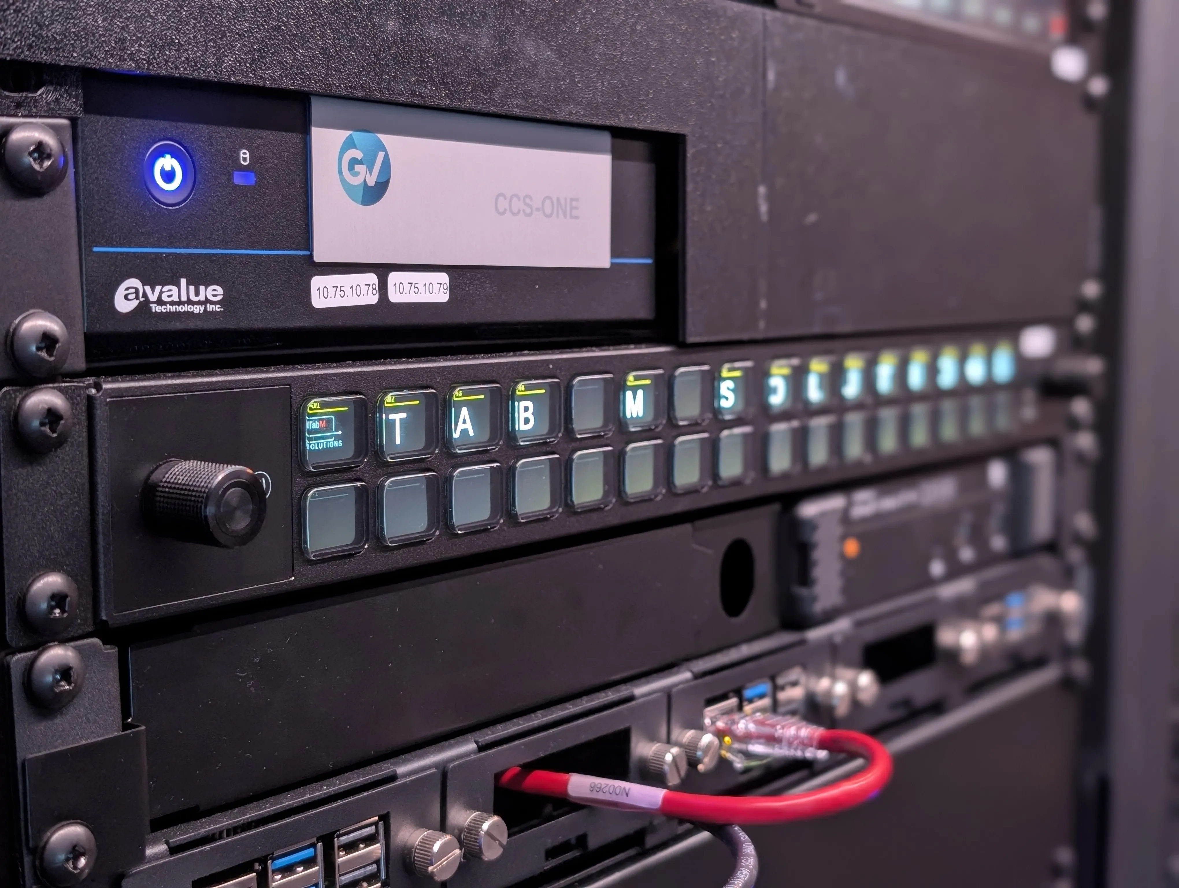 Close-up of a custom rack-mounted control panel with illuminated buttons showing Tab M Solutions branding on broadcast equipment.