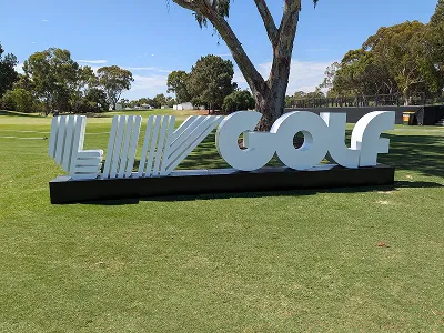 Large white Liv Golf sign on a green golf course with trees and a clear blue sky.