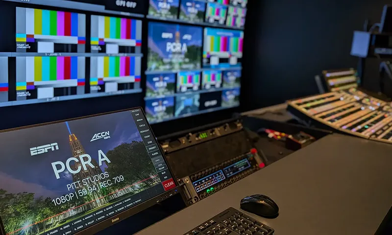 Broadcast control room with multiple monitors displaying test patterns and live video feeds, alongside a keyboard and control panels.