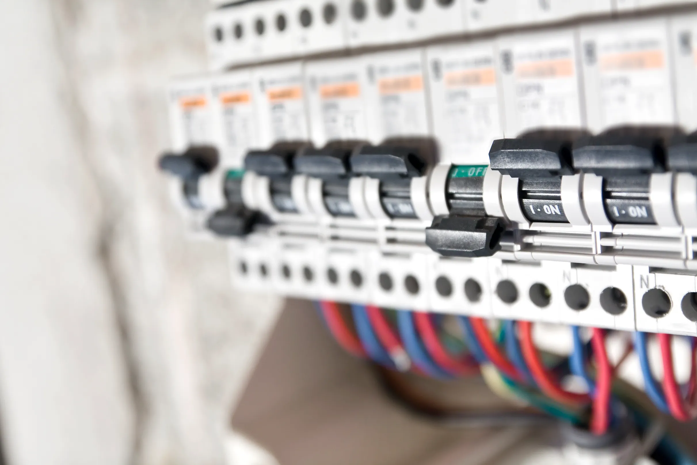 A close-up, side view of a row of white circuit breakers with switches in the "ON" position, connected to colorful wires.