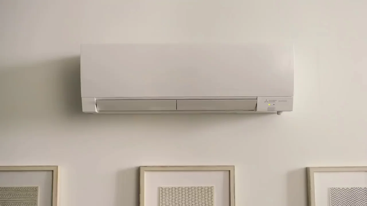 A white Mitsubishi Electric ductless mini-split indoor unit mounted high on a light-colored wall above three framed pictures.