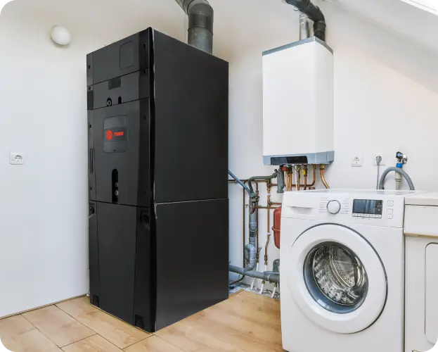 A large black Trane HVAC air handler and a white wall-mounted boiler next to a washer and dryer in a utility room.