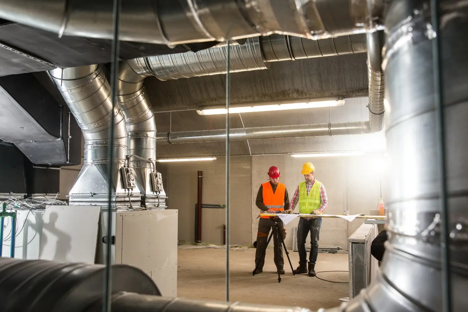Construction workers inspecting large ventilation ductwork.