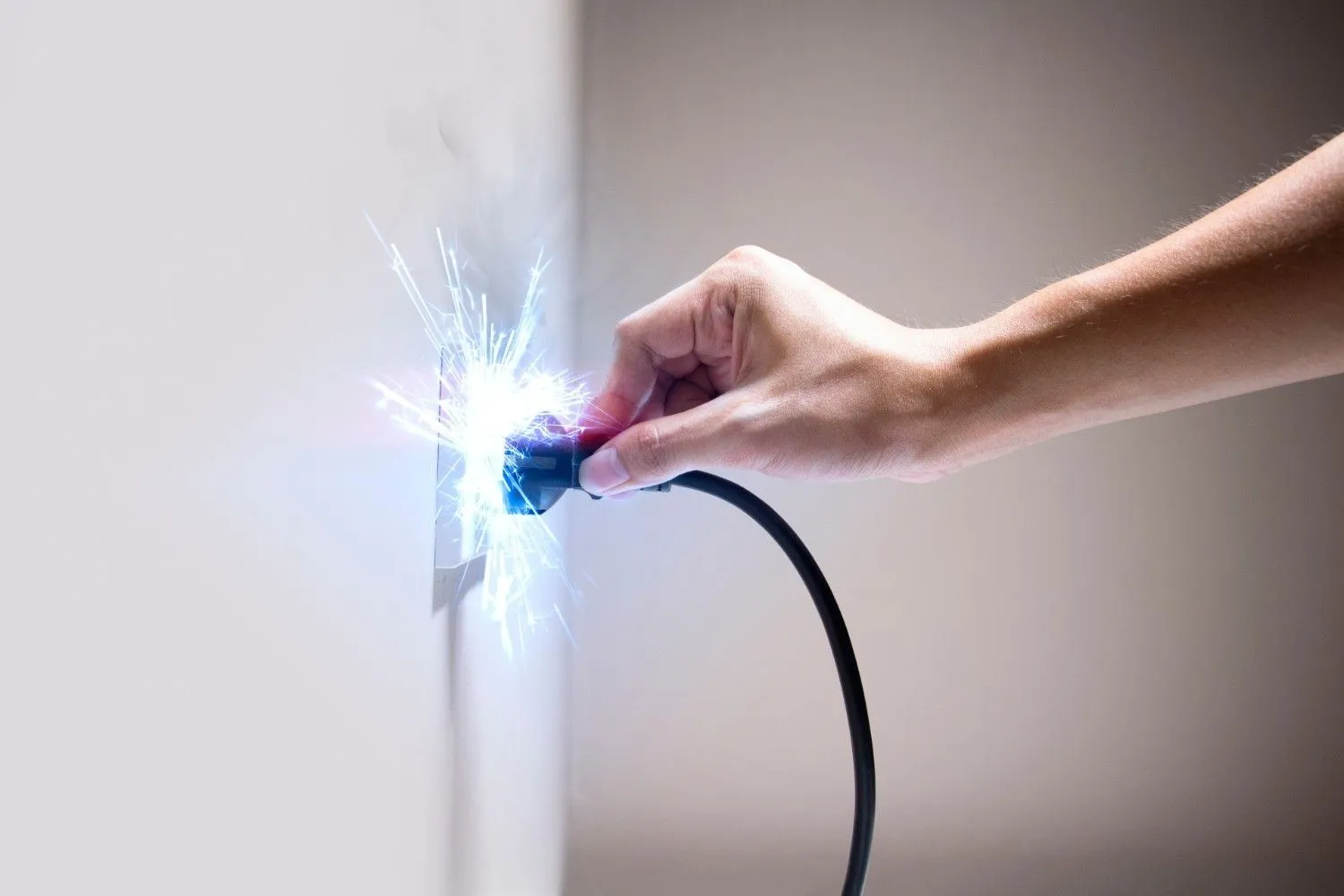 an electrical arc flash or short circuit, which occurs when current jumps through the air or takes an unintended, low-resistance path. The visible sparks and light are intense and represent a sudden, dangerous release of electrical energy. This usually happens due to faulty wiring, a damaged plug or outlet, or when a plug is inserted or removed carelessly or improperly under a heavy load. Such an event can cause significant damage to electronics, pose a serious fire hazard, and result in severe electric shock or burns to the person involved.