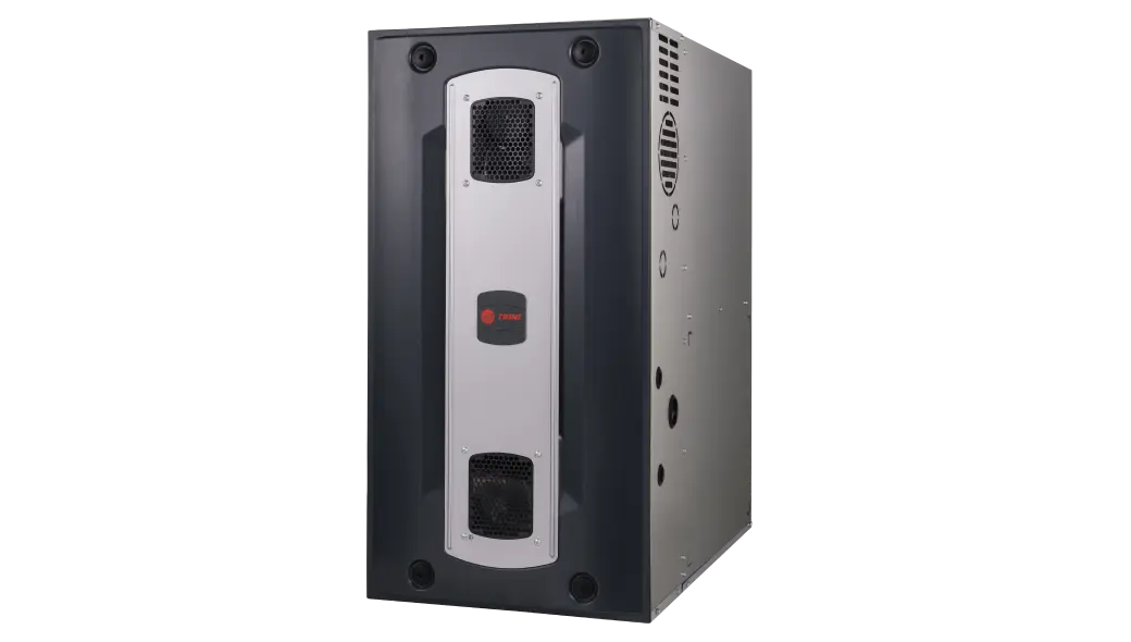 Trane brand furnace or air handler.  It has a large, rectangular, dark gray or black cabinet with a central, vertical, metallic silver panel. The silver panel features a red Trane logo in the middle and has two perforated or mesh grille sections, one at the top and one at the bottom, which likely serve as air intakes or access points. The overall design is modern and industrial.