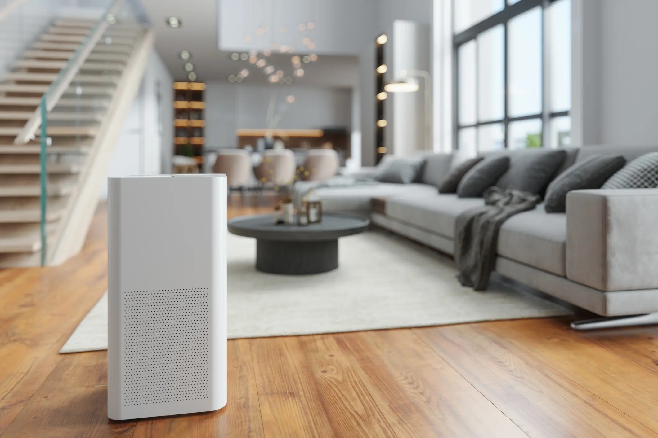 A modern, tall, white appliance in the foreground, likely a portable dehumidifier or air purifier, standing on a glossy wood floor.