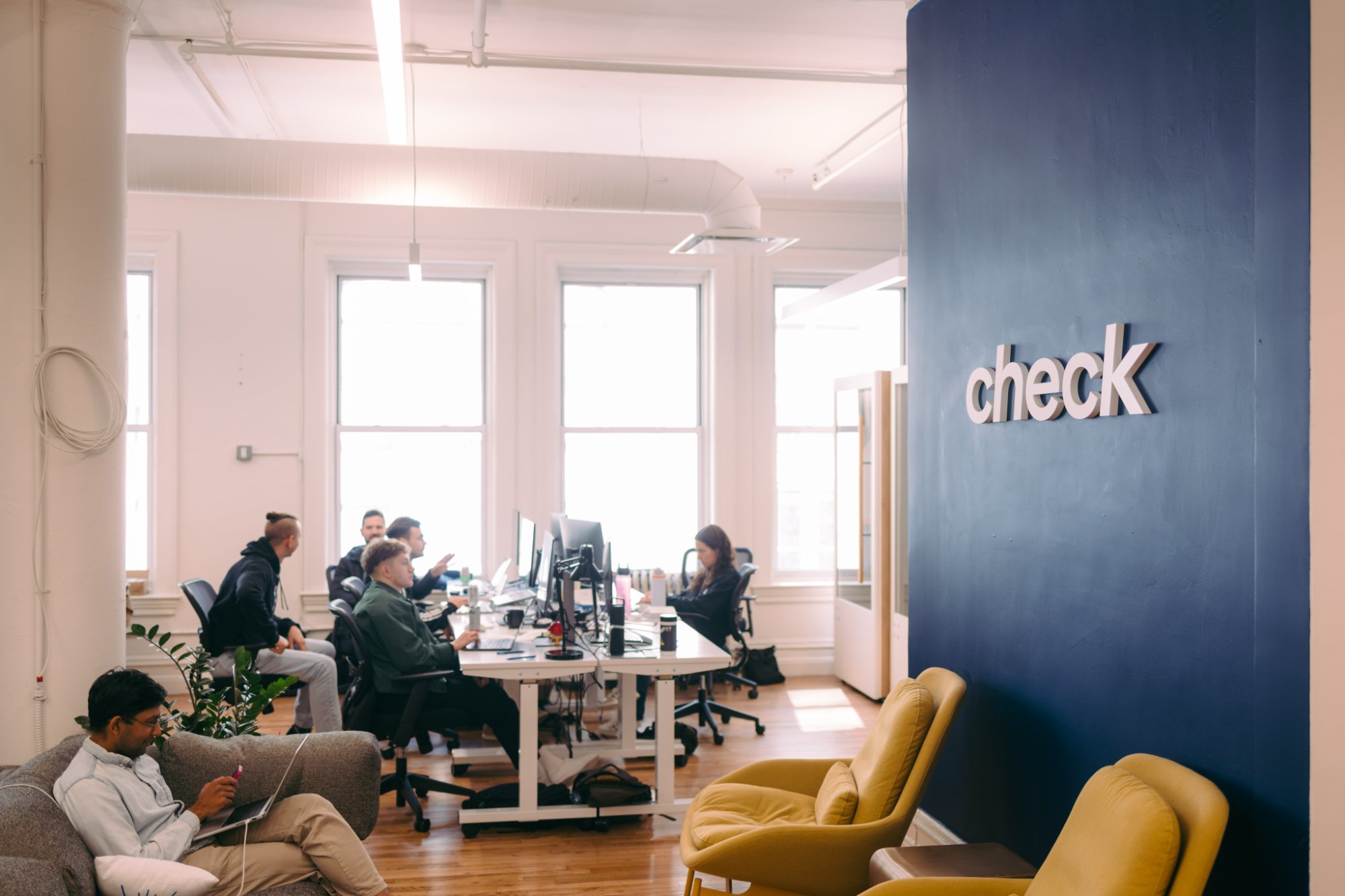 Check team working in the New York office beside the Check logo wall