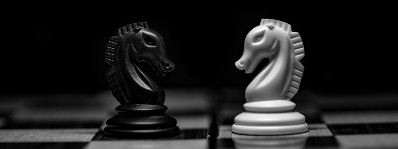 Black and white photo of a black knight and a white knight chess piece facing each other, symbolizing strategy and confrontation.