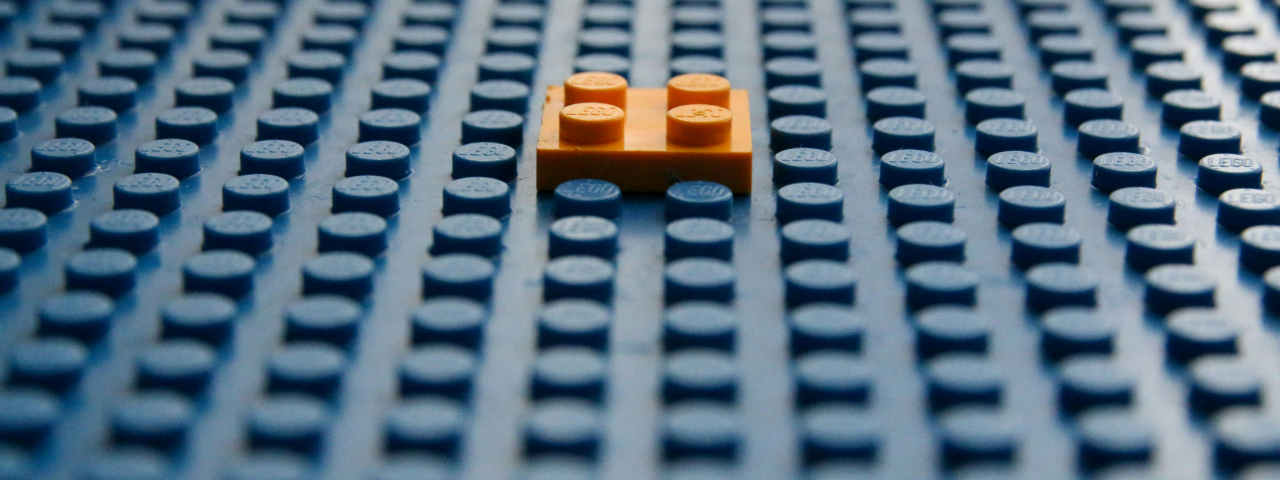 Single yellow Lego piece on a blue grid, symbolizing modular structure and extensibility.