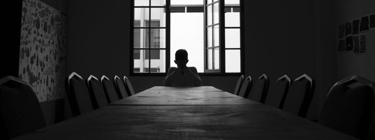 Frustrated person sitting alone at a long table, representing entrepreneurs starting with products instead of solving real pain.