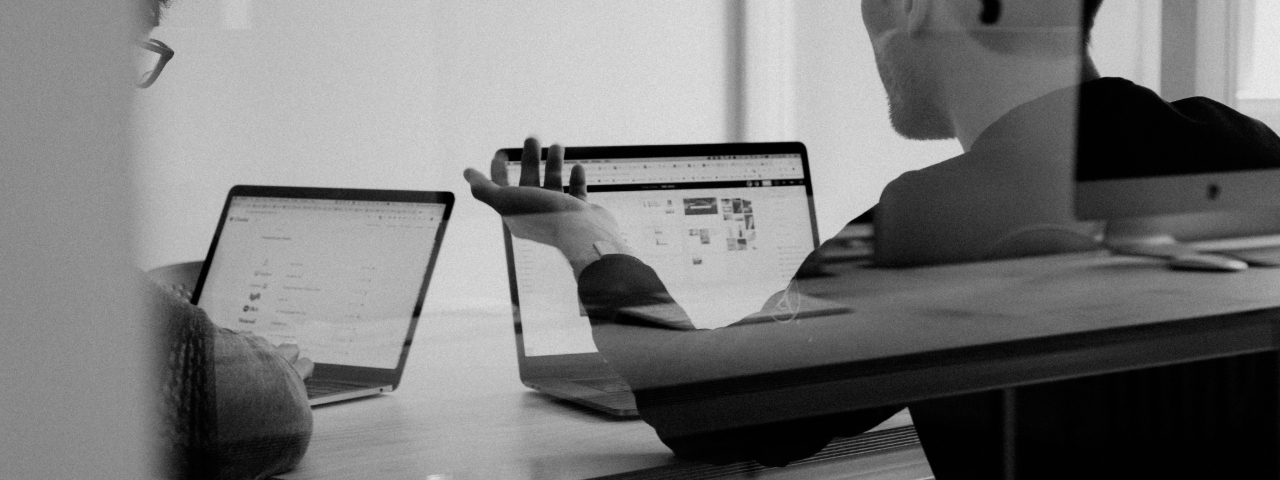 Black and white photo of two people working on laptops, reviewing a Shopify store layout or analytics dashboard