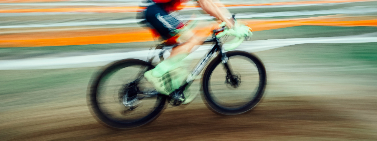 Motion-blurred image of a cyclist riding a mountain bike at high speed on a dirt track.