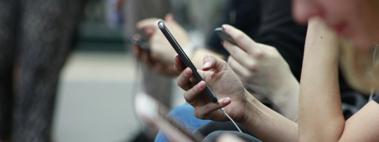 Close-up of several people sitting and using smartphones, focusing on their hands and devices.