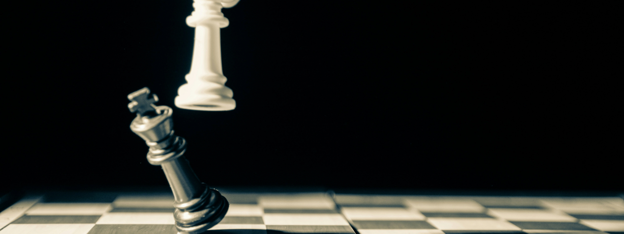 White chess king toppling a black king on a chessboard, symbolizing victory or checkmate.