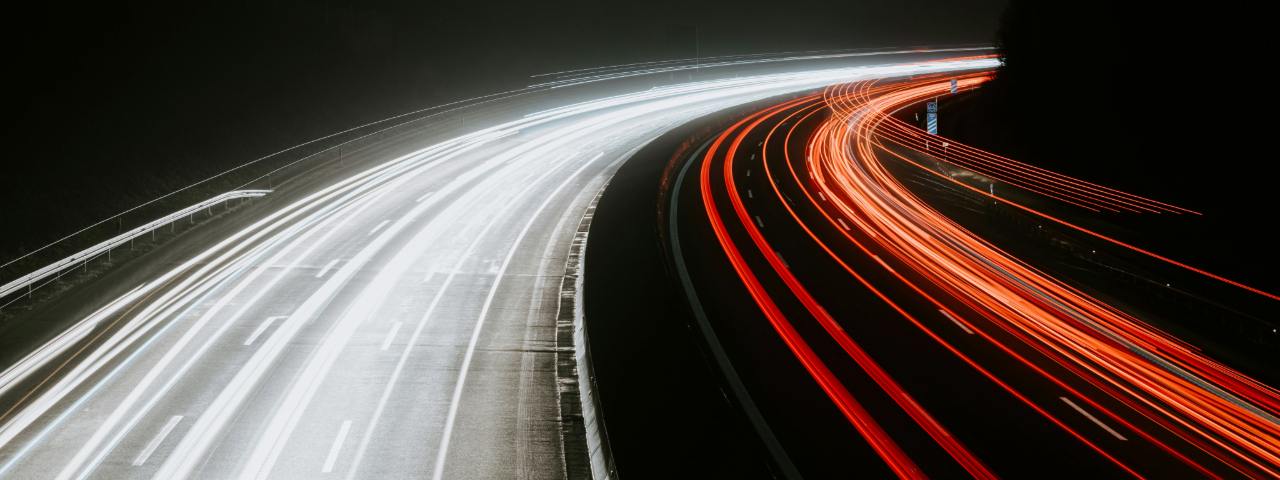 Long-exposure photo of a highway at night, showing light trails from vehicles in white and red.