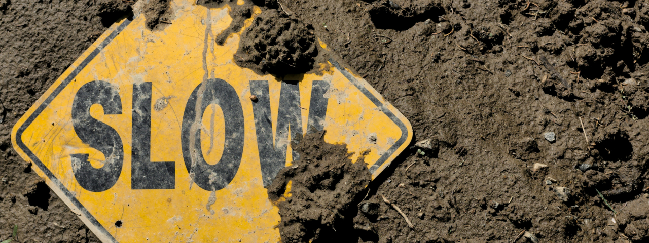 Yellow 'SLOW' caution sign partially covered in mud.