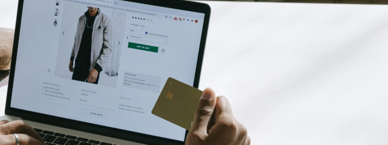 Person browsing an online store on a laptop while holding a credit card, showing product page UX.
