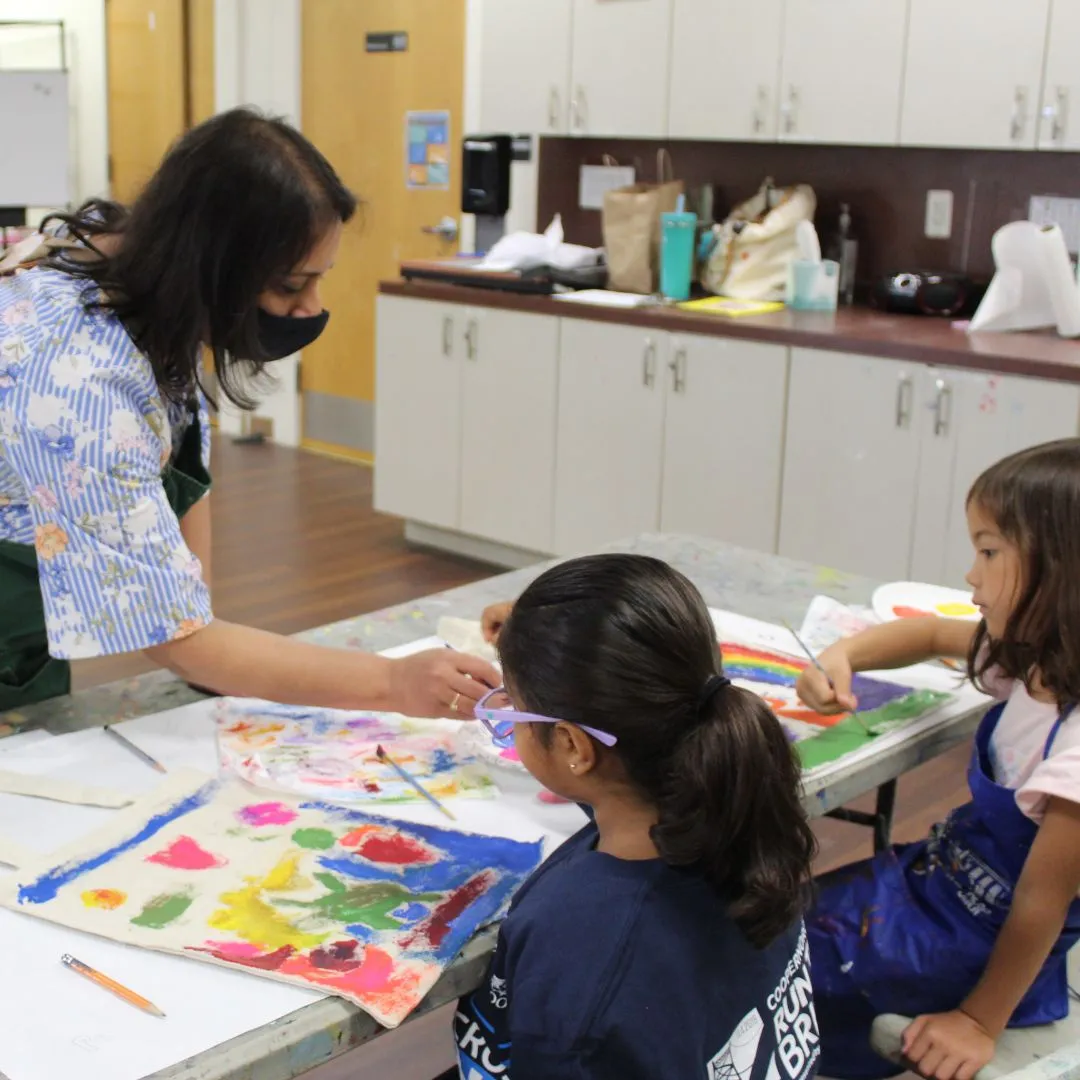 Ms. Anusha helps two students with their tote bag canvas paintings