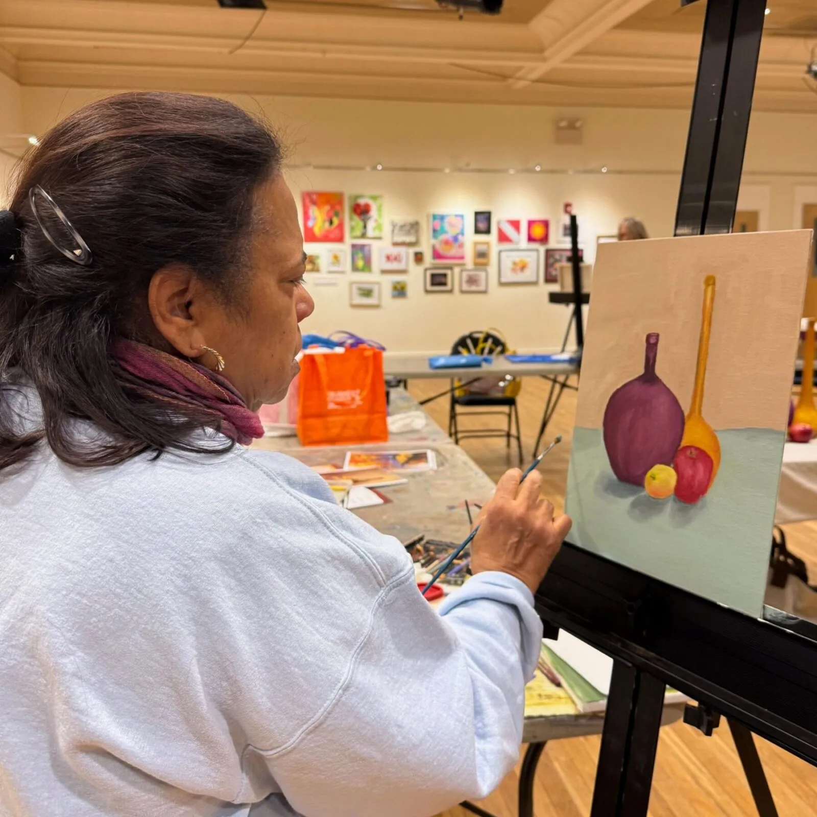 woman creates an oil painting still life with purple, red, and yellow fruits and vases