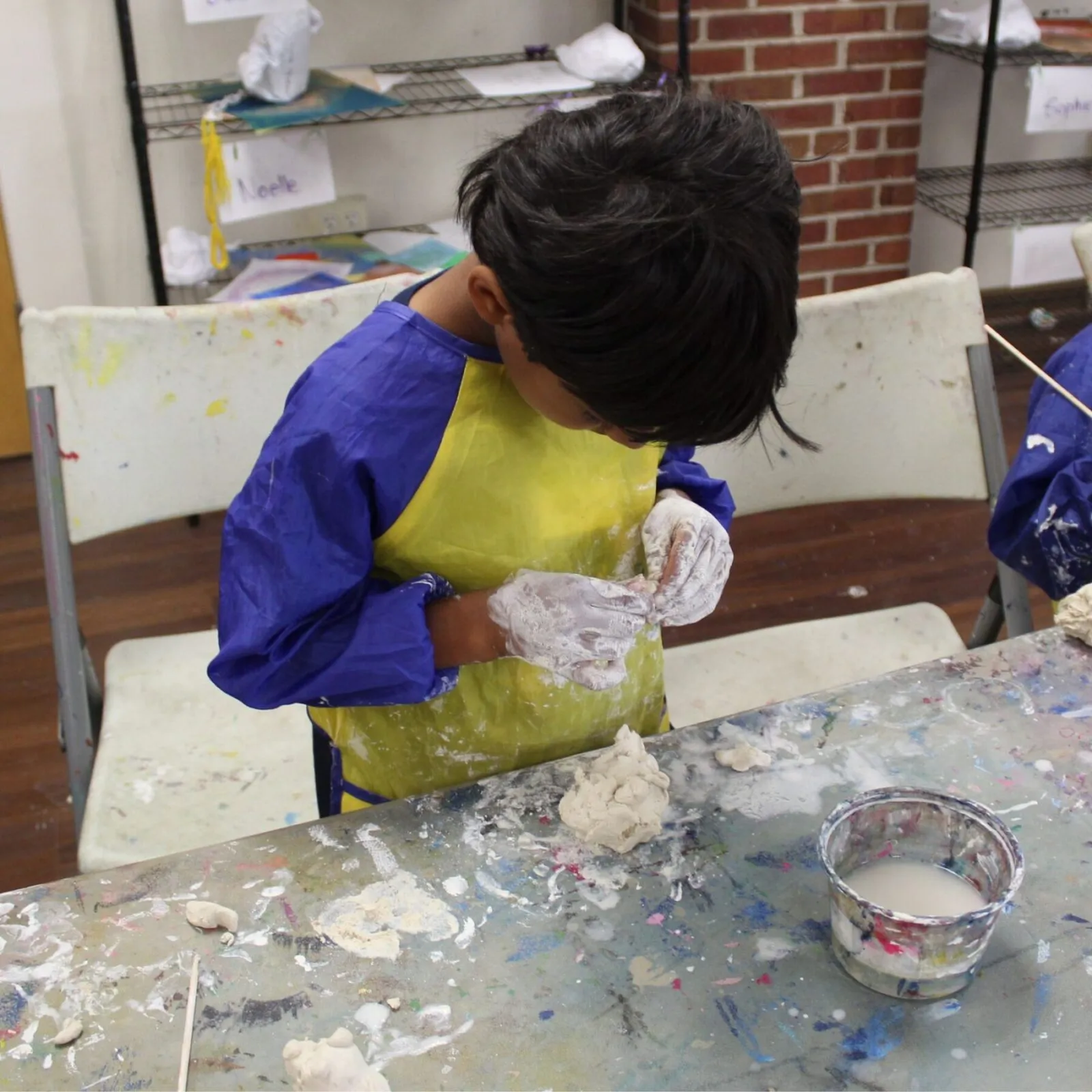 Child in blue and yellow smock uses clay tool