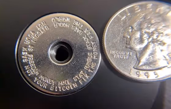 Titanium washer with engraved Bitcoin seed phrase words next to a U.S. quarter for size comparison.