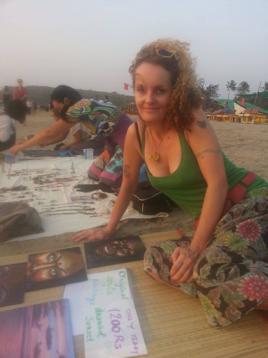 a woman sitting on the beach market with her paintings