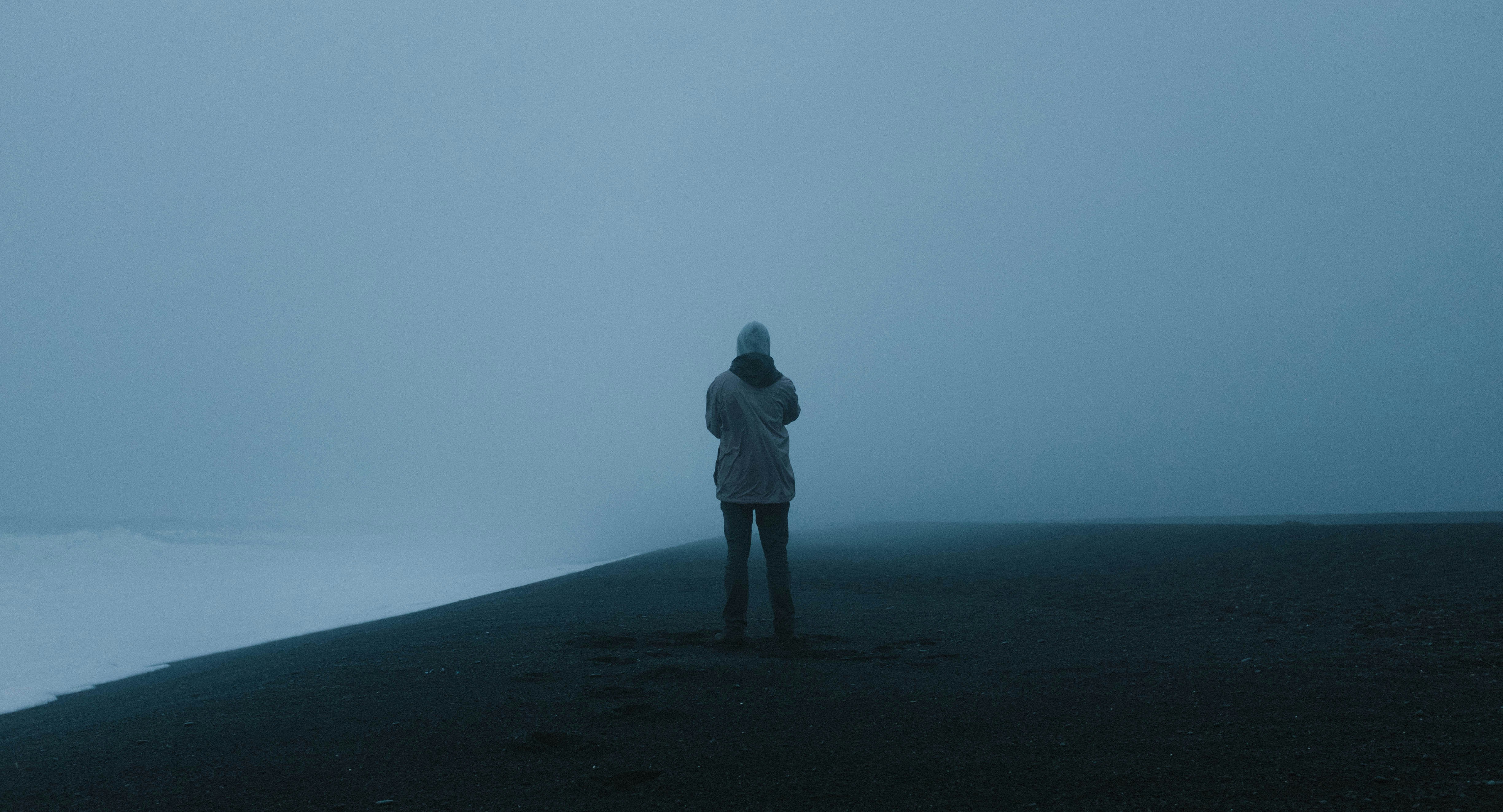 A man in cold weather gear staring into the distance alone. 
