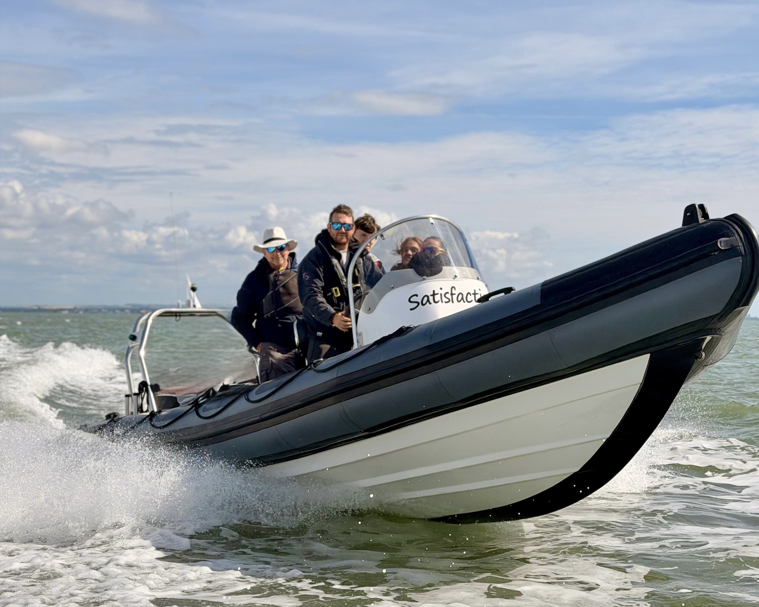 A black and white rigid inflatable powerboat speeding on water with people on board wearing jackets and sunglasses.
