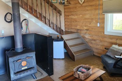 Cozy cabin interior with a wood-burning stove, wooden staircase, armchair, and a wooden coffee table with a basket.