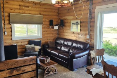 Cozy cabin interior with a sofa, armchair, wooden coffee table, and wooden chairs near a window and glass door.