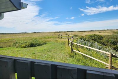 View of a grassy field with a wooden fence under a blue sky with scattered clouds.