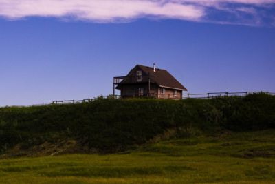 Wooden cabin on a grassy hill under a blue sky with scattered clouds.